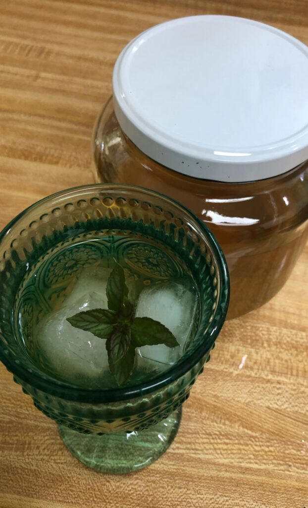 Mint tea in a blue glass with ice and a sprig of mint a jar of Sun Mint Tea