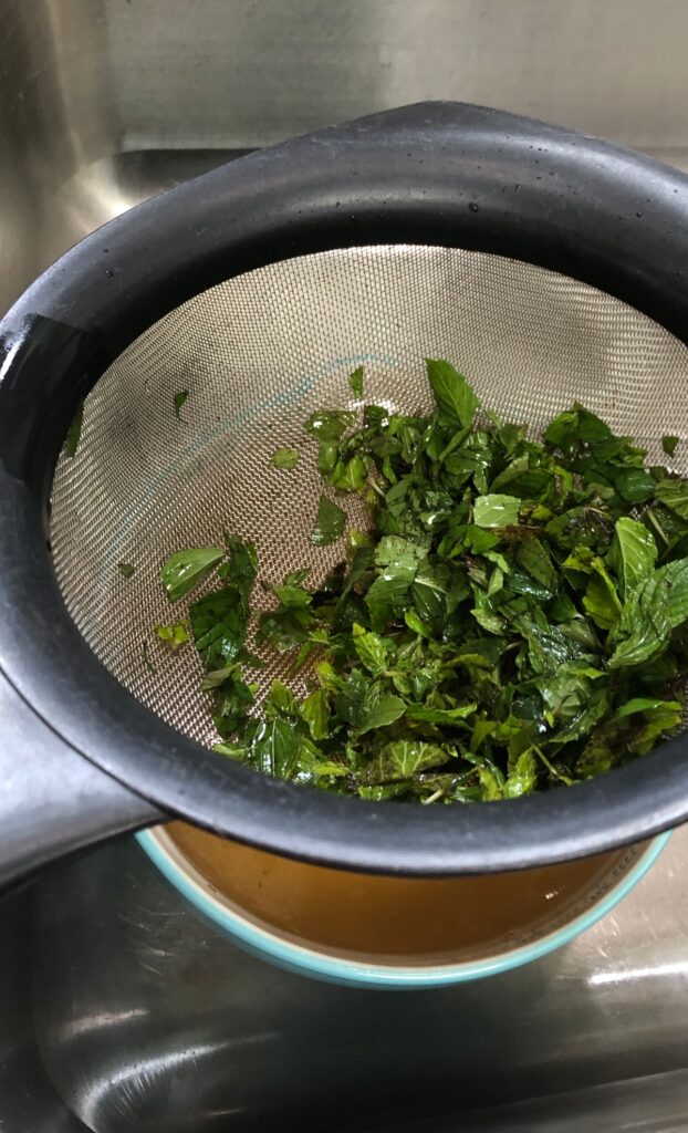 straining mint and mint tea into a bowl with a spout
