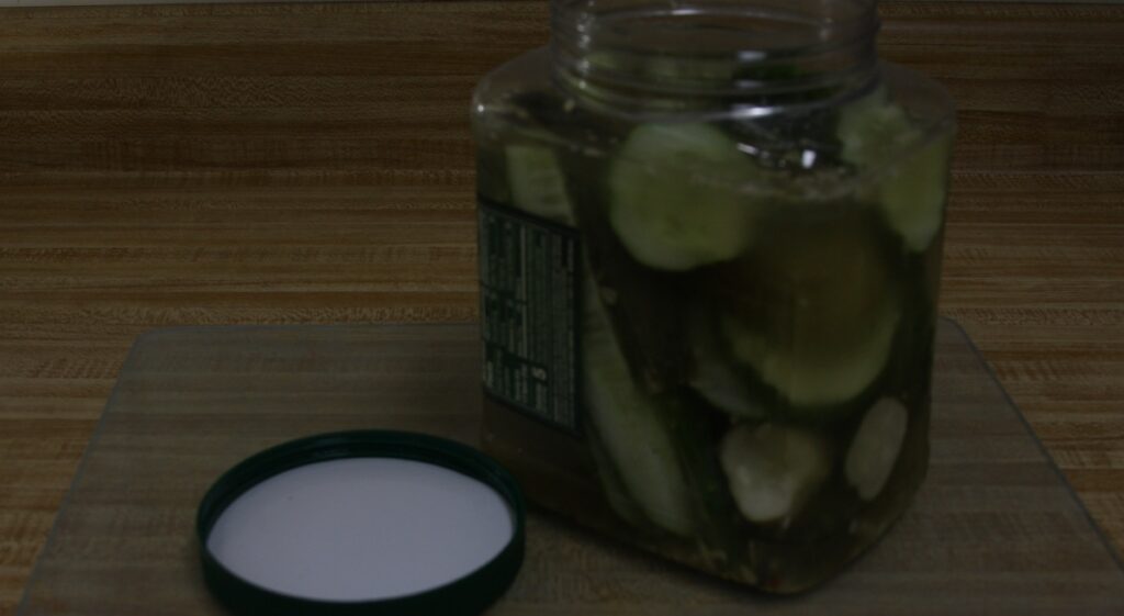 pickles various cuts in large plastic jar with lid on counter