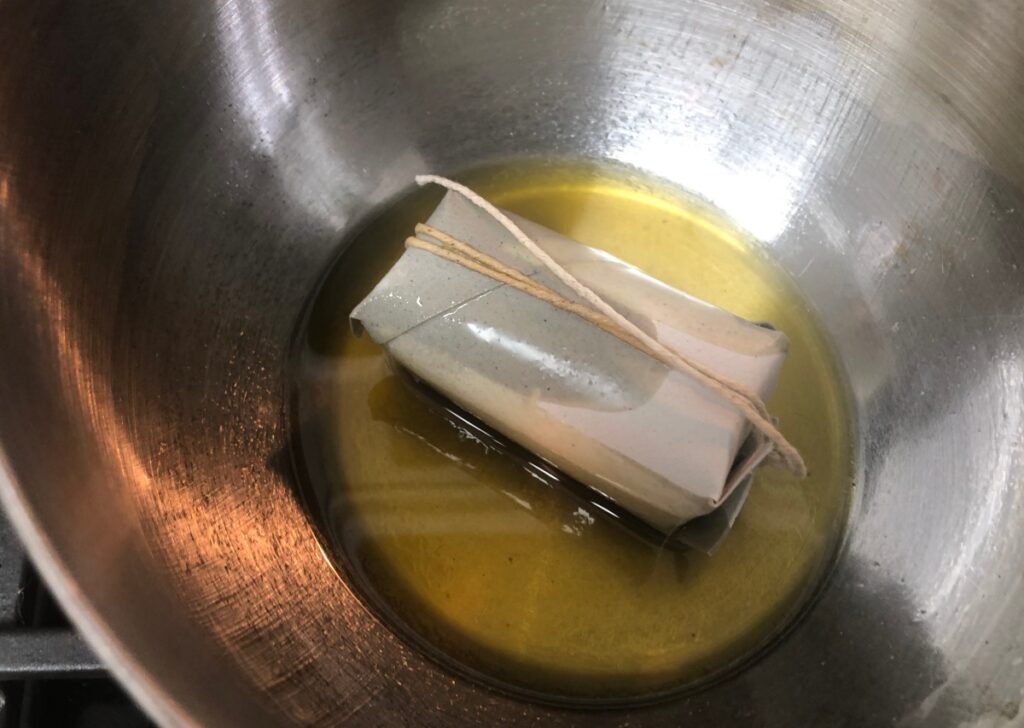 melted beeswax in heat proof bowl in water in sauce pan on stove empty toilet paper tube filled with dryer lint and herbs tied with string